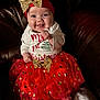 baby, smiling, red_skirt, gold_bow, headband, christmas, holiday_outfit, seated, leather_couch, infant, happy, cute, festive_clothing, tutu, sparkly, small_feet, long_sleeve_shirt, indoors, portrait, child