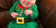 Ember joined the competition — help win amazing prizes! baby, child, smiling, green_clothing, striped_leggings, festive_outfit, elf_costume, leather_couch, indoor, cute, happy, portrait, sitting, infant, small_hands, barefoot, cozy, holiday, cheerful, young