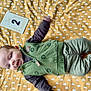 baby, infant, smiling, green_clothing, yellow_blanket, cloud_pattern, lying_down, card, two_months, happy, child, cute, portrait, indoors, soft_texture, young, raising_arm, casual_wear, vest, pants