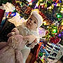 Covelea is registered to the contest to win money with this photo: baby, child, christmas_tree, holiday_lights, gift_wrapping, present, stuffed_animal, plush_toy, winter_clothing, hat, white_outfit, carpet, chair, indoors, festive, holiday_decor, tinsel, ornament, smiling, cute