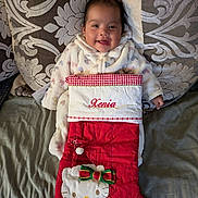 Xenia is registered to the contest to win money with this photo: baby, bed, blanket, child, christmas_stocking, couch, cute, embroidered_name, fabric, hand, happy, hello_kitty, holiday, indoors, infant, onesie, patterned_pillow, portrait, red_stocking, smiling