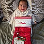 baby, bed, blanket, child, christmas_stocking, couch, cute, embroidered_name, fabric, hand, happy, hello_kitty, holiday, indoors, infant, onesie, patterned_pillow, portrait, red_stocking, smiling