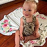 toddler, child, baby, smiling, sitting, blanket, floral, hair_bows, overalls, camouflage, floor, wooden_floor, indoors, cute, happy, person, portrait, skin, face, blue_eyes