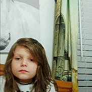 Cora is registered to the contest to win money with this photo: child, bed, blanket, curtain, painting, horse, indoor, person, long_hair, serious, furniture, window, home, portrait, casual, sitting, cozy, red_blanket, white_shirt, decor