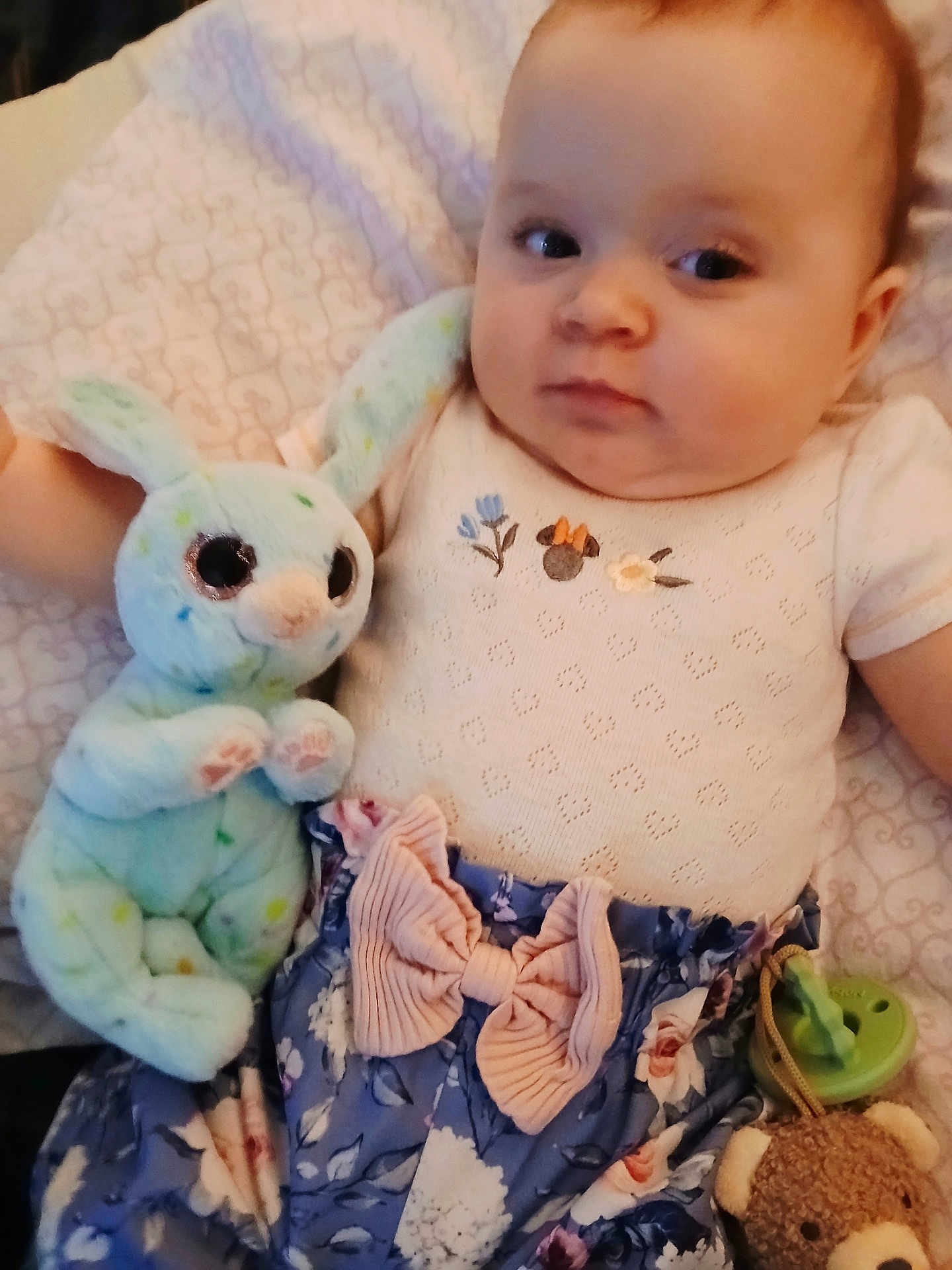 Leah joined the competition — help win amazing prizes! baby, plush_toy, bunny, pacifier, teddy_bear, blanket, patterned_clothing, bow, infant, cute, soft_toy, child, lying_down, face, looking_sideways, blue, pink, floral, indoor, portrait