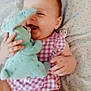 baby, infant, plush_toy, stuffed_animal, purple_clothing, smiling, happy, lying_down, blanket, cute, child, soft_toy, indoor, toddler, giggling, close_up, hands, face, cozy, patterned