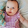 baby, child, infant, stuffed_animal, plush_toy, purple_dress, checkered_pattern, blue_eyes, smiling, cute, lying_down, blanket, heart_pattern, soft_toy, indoor, portrait, young_child, happy, close_up, adorable