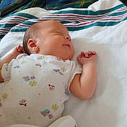 Leah is registered to the contest to win money with this photo: baby, newborn, sleeping, blanket, onesie, clothing, infant, face, peaceful, bed, plaid, remote_control, soft, resting, cute, person, skin, arm, hand, indoors