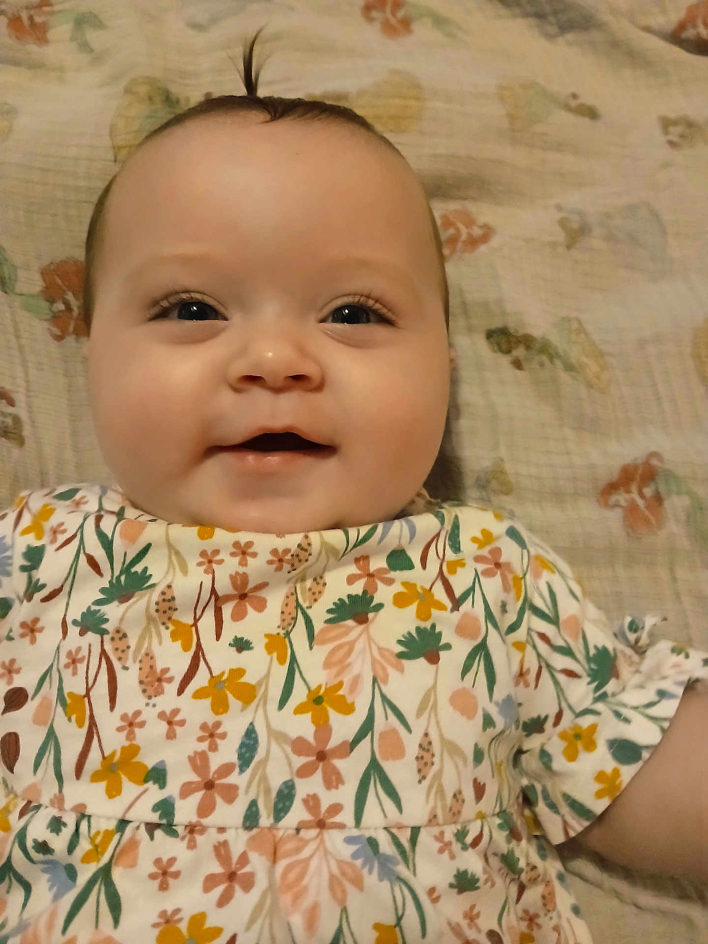 Leah is registered to the contest to win money with this photo: baby, child, smiling, face, portrait, infant, cute, floral_dress, patterned_clothing, lying_down, blanket, happy, young_child, indoors, skin, head, eyes, small_hair_tuft, cheeks, person