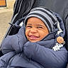 Owen participe au concours pour gagner de l'argent avec cette photo : child, toddler, stroller, winter_clothing, jacket, beanie, smile, face, outdoor, cold_weather, baby_accessory, pacifier, black_stroller, cute, cozy, happy, person, infant, playful, hands