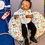 baby, infant, medical_equipment, breathing_tube, pillow, floral_pattern, carpet, sneakers, black_pants, white_shirt, bib, face, child, lying_down, indoors, healthcare, monitor, cable, footwear, person