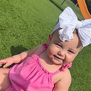 Blakeley is registered to the contest to win money with this photo: baby, child, girl, outdoor, playground, grass, pink_clothing, headband, white_bow, smiling, sunlight, happy, cute, infant, summer, play, park, young_child, person, nature