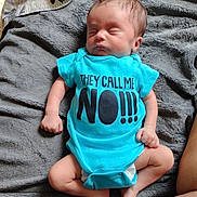 Mateo is registered to the contest to win money with this photo: baby, infant, sleeping, onesie, blue_clothing, blanket, soft_texture, cute, peaceful, child, newborn, human, person, indoors, resting, toddler, text_on_clothing, casual, skin, hands