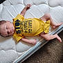 Mateo is registered to the contest to win money with this photo: baby, newborn, infant, sleeping, yellow_onesie, text_on_clothing, mattress, carpet, hand, foot, face, person, child, cute, resting, indoors, clothing, sleep, lying_down, humor