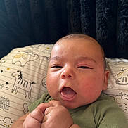 Joe Michale Segura is registered to the contest to win money with this photo: baby, infant, child, face, hands, pillow, animal_print, green_shirt, closeup, portrait, indoors, cute, expression, skin, head, newborn, lying_down, soft_background, sleepy, fist