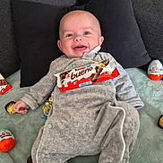 Aylann a rejoint le concours — aidez-le/la à gagner de superbes lots ! baby, smiling, infant, onesie, gray_clothing, pillow, couch, blanket, chocolate, kinder_bueno, kinder_egg, ferrero_rocher, food, sweet, snack, happy, indoors, person, head, face