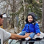 Jesse joined the competition — help win amazing prizes! toddler, child, adult, blue_jacket, hood, smiling, car_roof, blanket, outdoor, winter, tree, fence, sunglasses, cap, tattoo, person, cold_weather, clothing, residential_area, supporting_hand