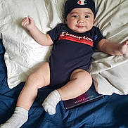Jesse is registered to the contest to win money with this photo: baby, child, infant, person, bed, pillow, blanket, clothing, sock, hat, smiling, face, cute, indoor, relaxing, apparel, text, logo, foot, skin