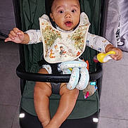 Isayah participe au concours pour gagner de l'argent avec cette photo : baby, bib, child, clothing, cute, expression, fabric, face, feet, floor, hand, indoor, infant, legs, person, playful, rattle, seat, stroller, toy