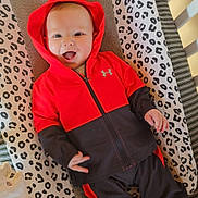 Isaac a rejoint le concours — aidez-le/la à gagner de superbes lots ! baby, child, hoodie, red_clothing, black_clothing, smiling, tongue_out, changing_pad, animal_print, striped_socks, striped_mat, indoor, infant, cute, playful, person, apparel, fabric, happy, lying_down