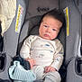 baby, infant, car_seat, blue_eyes, white_outfit, knit_hat, hands, face, hair, indoor, child, clothing, seatbelt, expression, person, newborn, cute, comfort, safety, portrait
