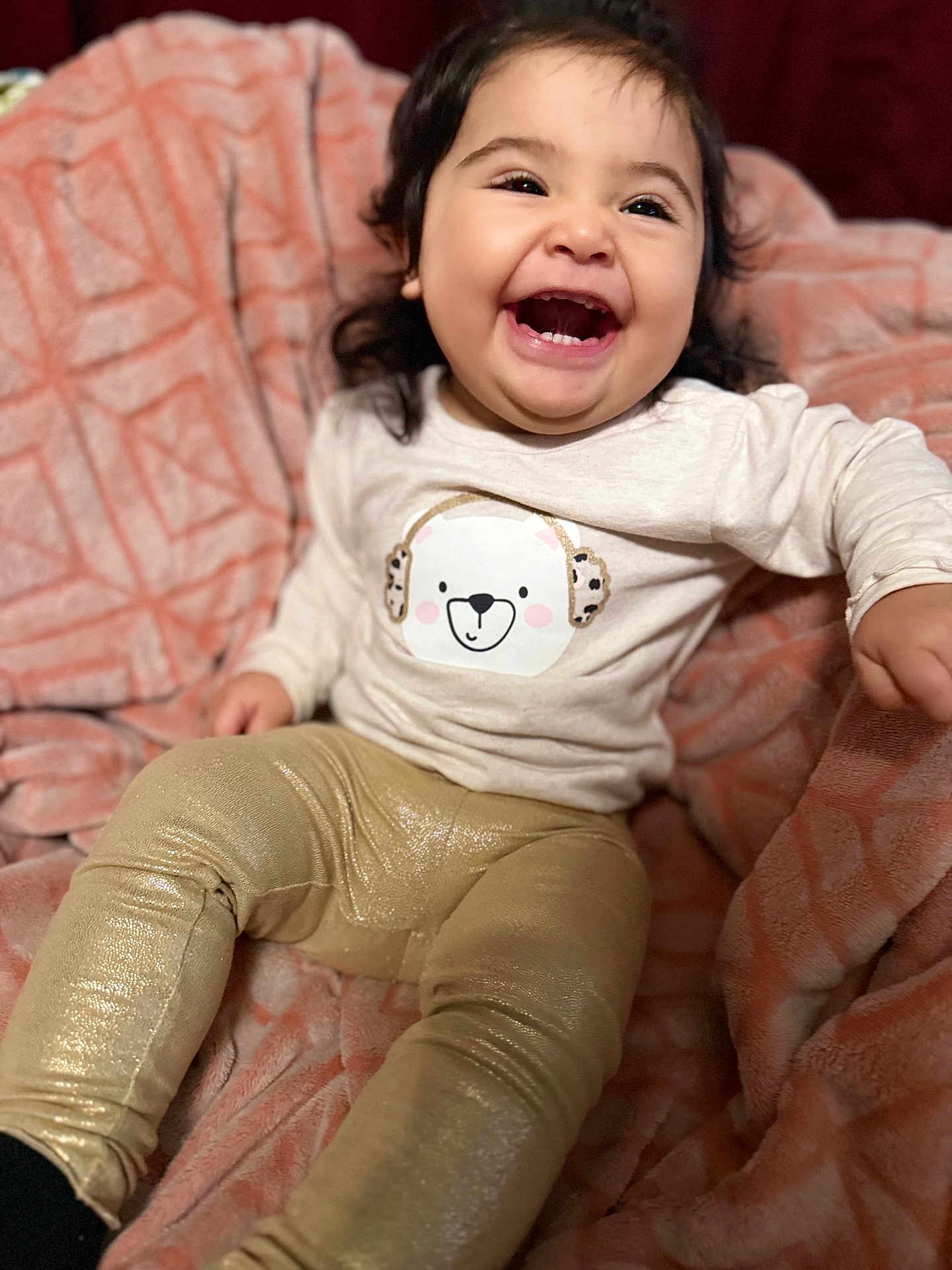 Aimee Sue is registered to the contest to win money with this photo: toddler, smiling, happy, child, face, clothing, leggings, shirt, bear_design, blanket, fabric, texture, indoors, cozy, cute, person, portrait, sitting, black_hair, cheerful