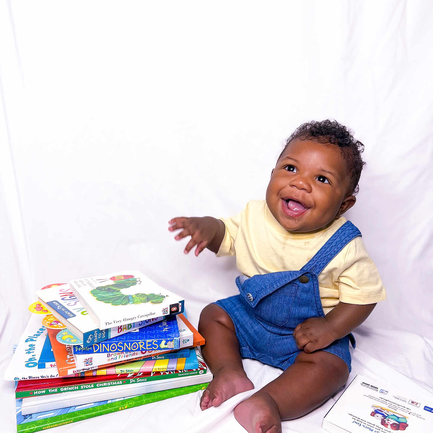 Khole is registered to the contest to win money with this photo: advertisement, baby, babylaughing, bodypart, book, clothing, face, finger, hand, happy, head, pants, person, photography, portrait, publication, reading, sitting, smile, t_shirt