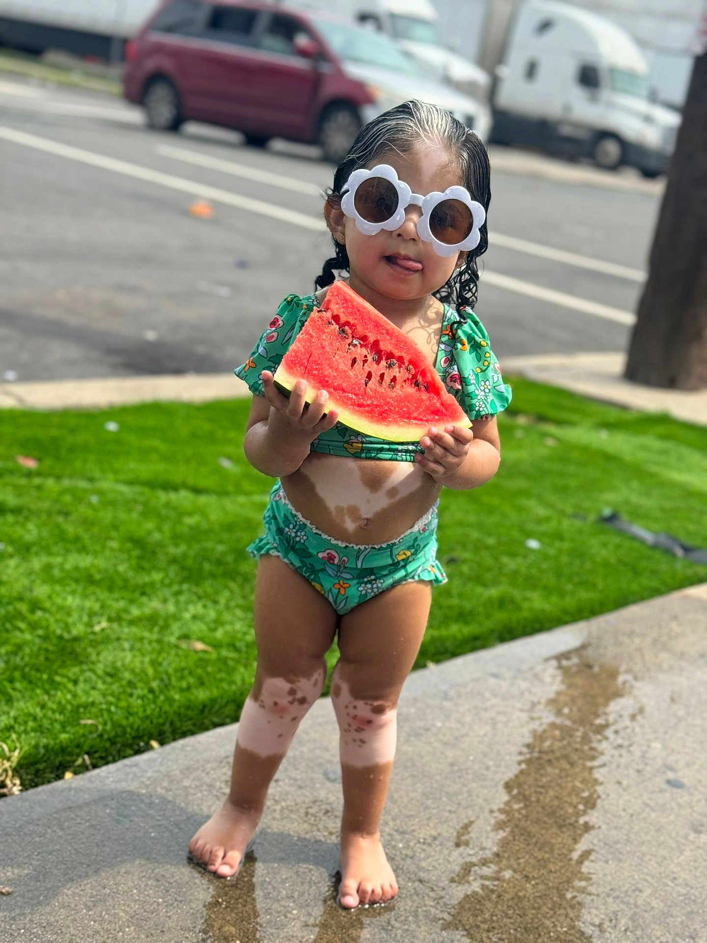 Júlia is registered to the contest to win money with this photo: toddler, child, watermelon, sunglasses, green_swimsuit, vitiligo, barefoot, sidewalk, grass, summer, outdoor, street, cute, fun, food, fruit, playful, standing, sunny, daytime