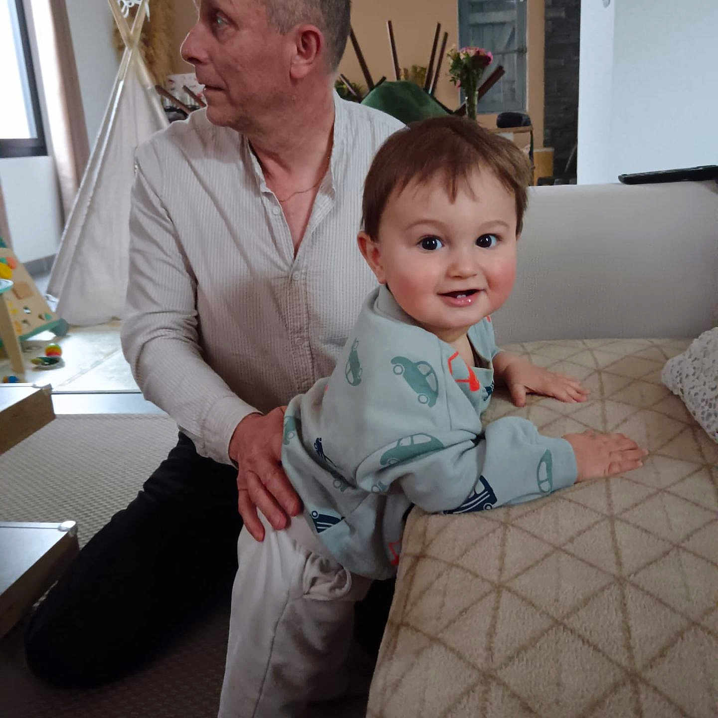 Roman a rejoint le concours — aidez-le/la à gagner de superbes lots ! adult, blanket, car_prints, child, couch, curtains, family, furniture, home_decor, indoor, living_room, man, pants, person, rug, smile, sweatshirt, toddler, toy, window