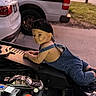 child, toddler, baby, boy, portrait, smiling, cap, backward_cap, denim_overalls, outdoor, car, vehicle, engine, car_engine, automotive, garage, driveway, parked_cars, daylight, candid_photography