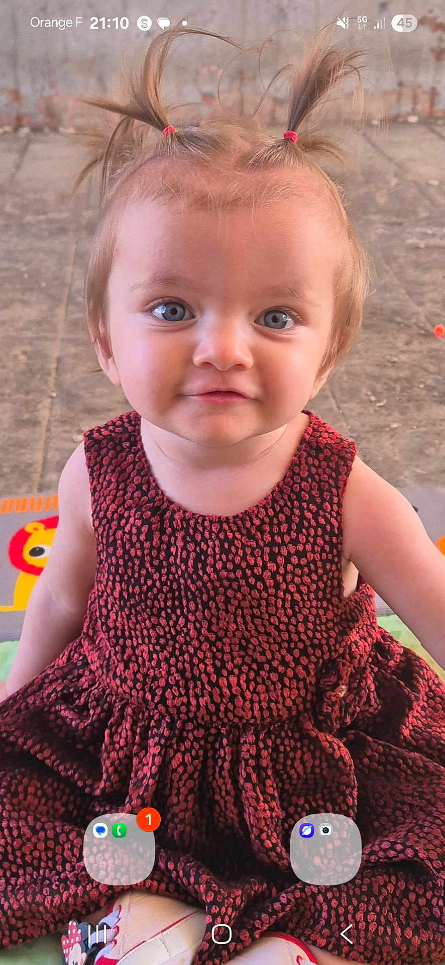 Mackenzie participe au concours pour gagner de l'argent avec cette photo : toddler, child, blue_eyes, pigtails, dress, red_dress, patterned_clothing, smiling, sitting, outdoor, concrete_floor, playful_hair, person, young_child, footwear, colorful_mat, cute, portrait, happy, baby