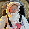baby, infant, stroller, onesie, hood, fuzzy_clothing, blue_eyes, pacifier, toy, straps, outdoor, sunlight, golden_hour, cute, child, face, person, winter_clothing, warm, soft