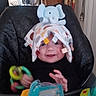 baby, child, high_chair, toy, blanket, elephant_plush, smiling, indoor, colorful, play, furniture, person, happy, cute, red_wheels, yellow_toy, blue_toy, hand, face, room