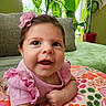 Isadora is registered to the contest to win money with this photo: baby, child, smiling, pink_clothing, headband, flower, cushion, floral_pattern, indoor, houseplant, greenery, portrait, cute, happy, infant, person, closeup, cozy, bright, home