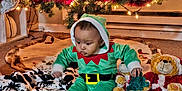D'Andre is registered to the contest to win money with this photo: baby, child, christmas_tree, holiday, elf_costume, plush_toy, teddy_bear, blanket, carpet, lights, ornament, decorations, festive, indoor, floor, cute, green_clothing, red_and_white, toy, sitting