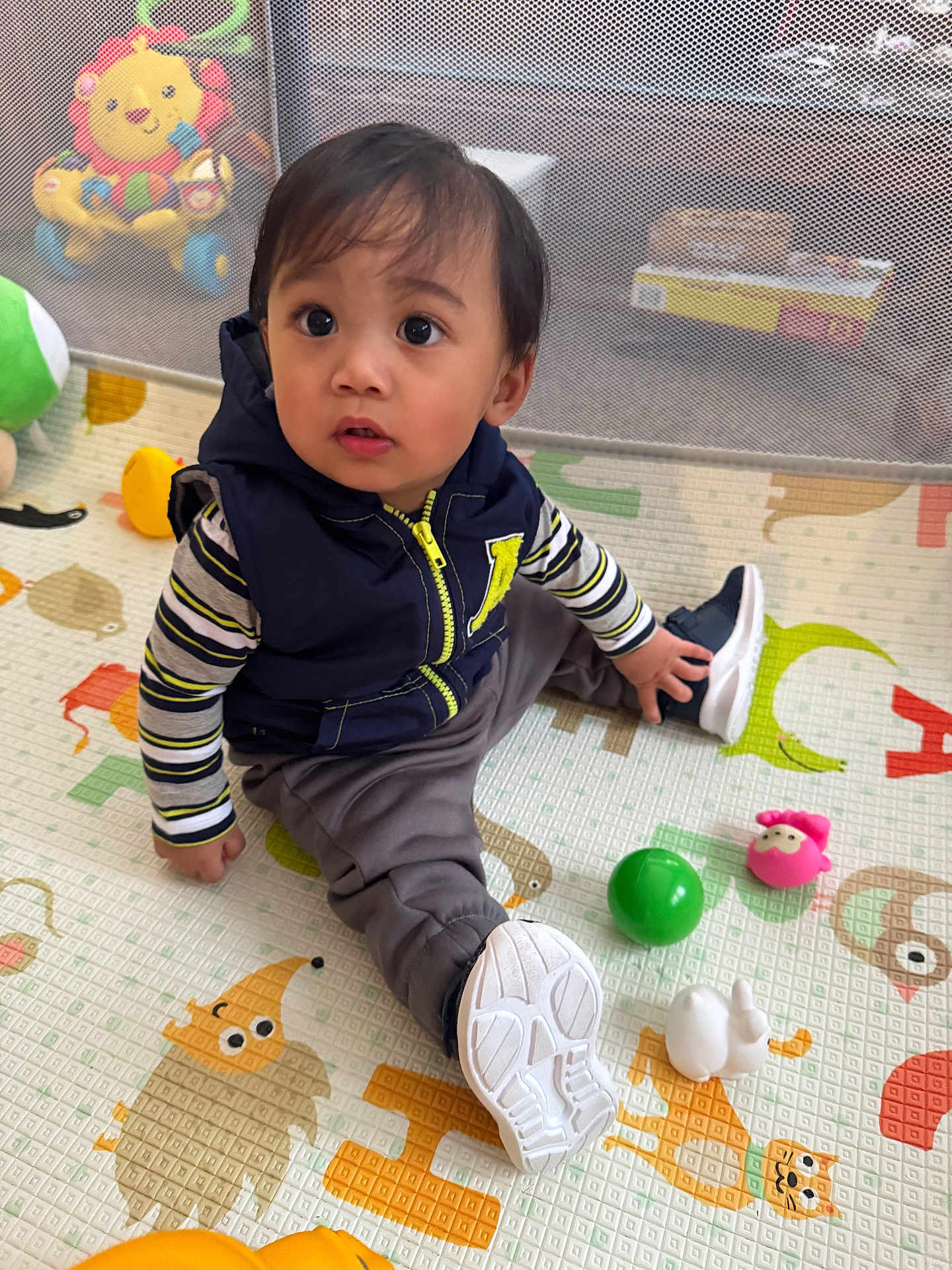 Kym is registered to the contest to win money with this photo: toddler, child, playmat, toy, sitting, curious, indoor, clothing, vest, striped_shirt, shoe, play_area, colorful, floor_mat, cute, expression, young_child, baby_toys, soft_toys, portrait