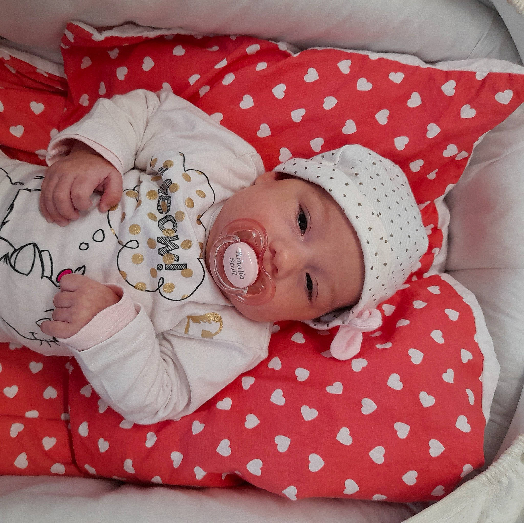 Amalia a rejoint le concours — aidez-le/la à gagner de superbes lots ! baby, baby_products, baby_safety, baby_sleeping, baby_toddler_clothing, bedding, child, comfort, face, facial_expression, headgear, headwear, linens, pattern, person, pink, room, skin, sleeve, textile