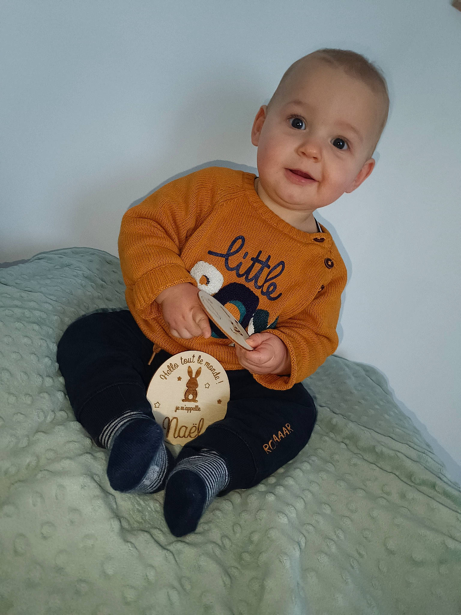 Naël participe au concours pour gagner de l'argent avec cette photo : arm, baby, baby_toddler_clothing, cheek, comfort, facial_expression, finger, hand, happy, linens, mammal, person, room, sitting, sleeve, smile, t_shirt, textile, toddler, toy
