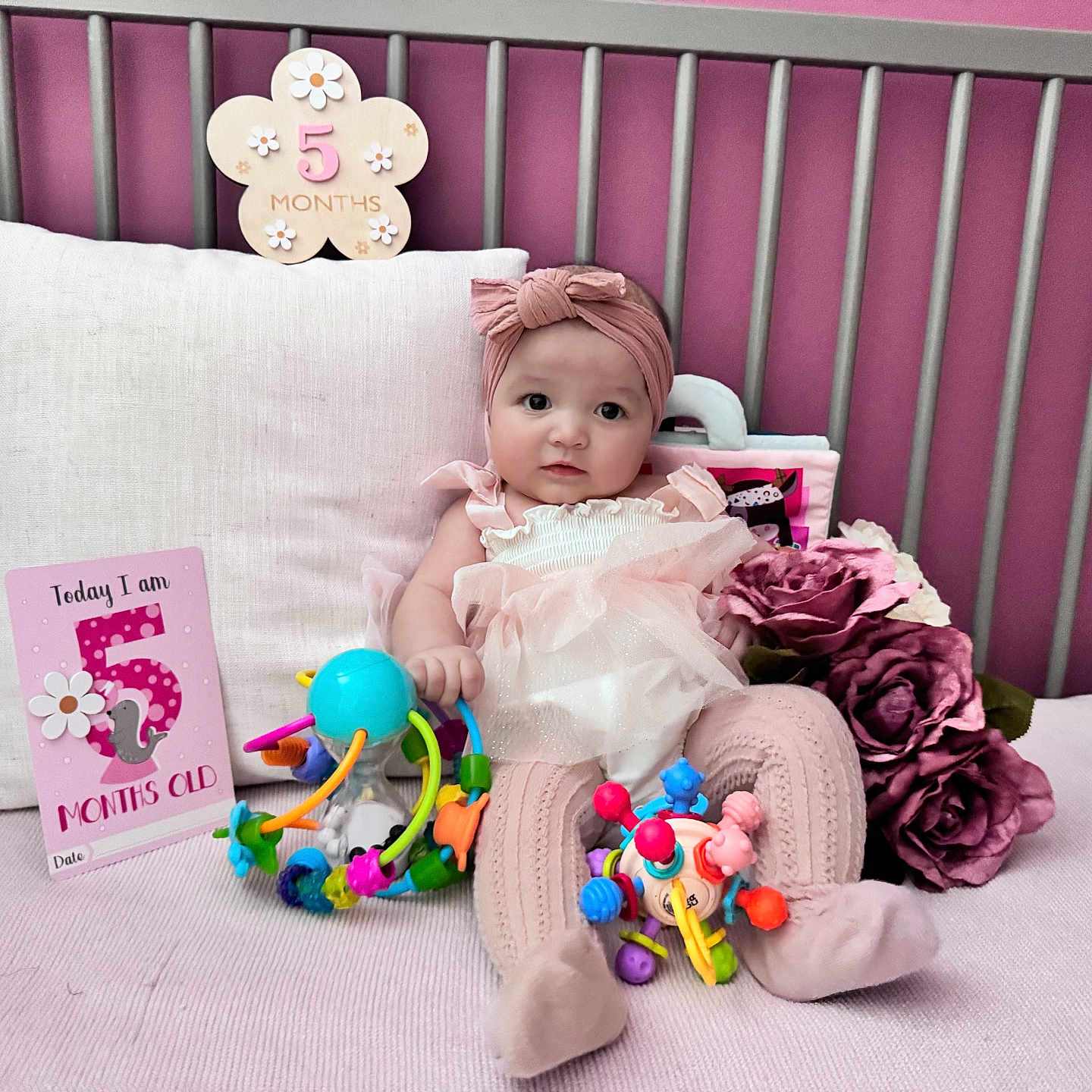 Mykha is registered to the contest to win money with this photo: baby, blanket, child, clothing, crib, cute, decor, face, flowers, girl, headband, indoor, infant, milestone_card, pillow, pink, portrait, sitting, soft_toys, toys