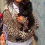 black_dog, braces, clothing, curly_hair, cute, dog, fur, hand, happy, holding, jacket, leopard_print, outdoor, person, pet, puppy, small_dog, smile, tail, wall