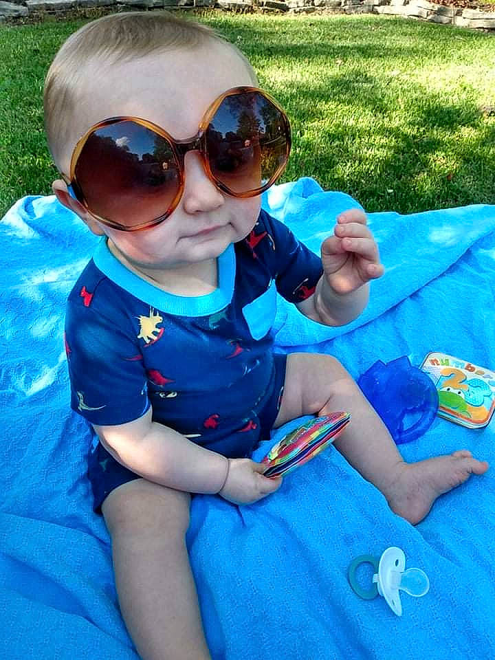Jameson is registered to the contest to win money with this photo: azure, baby_toddler_clothing, blue, cool, eyewear, facial_expression, finger, fun, glasses, goggles, grass, green, hand, happy, light, person, plant, sleeve, sunglasses, toddler