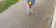 Maël participe au concours pour gagner de l'argent avec cette photo : child, barefoot, yellow_bandana, red_sunglasses, toy_gun, blue_shirt, pants, outdoor, grass, concrete_path, gate, rural, dirt_road, playful, smiling, person, daylight, casual, fun, summer
