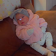 Blossom is registered to the contest to win money with this photo: baby, child, infant, couch, brown_couch, pink_jacket, headband, butterfly_sticker, indoor, cozy, warm_lighting, white_pants, sitting, cute, portrait, furniture, soft_texture, relaxing, young_child, home