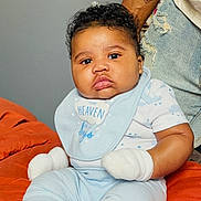 Demetrius joined the competition — help win amazing prizes! baby, infant, blue_clothing, mittens, bib, tattoo, adult_arm, orange_blanket, indoor, portrait, cute, child, sitting, face, expression, soft_lighting, denim, casual, skin, person
