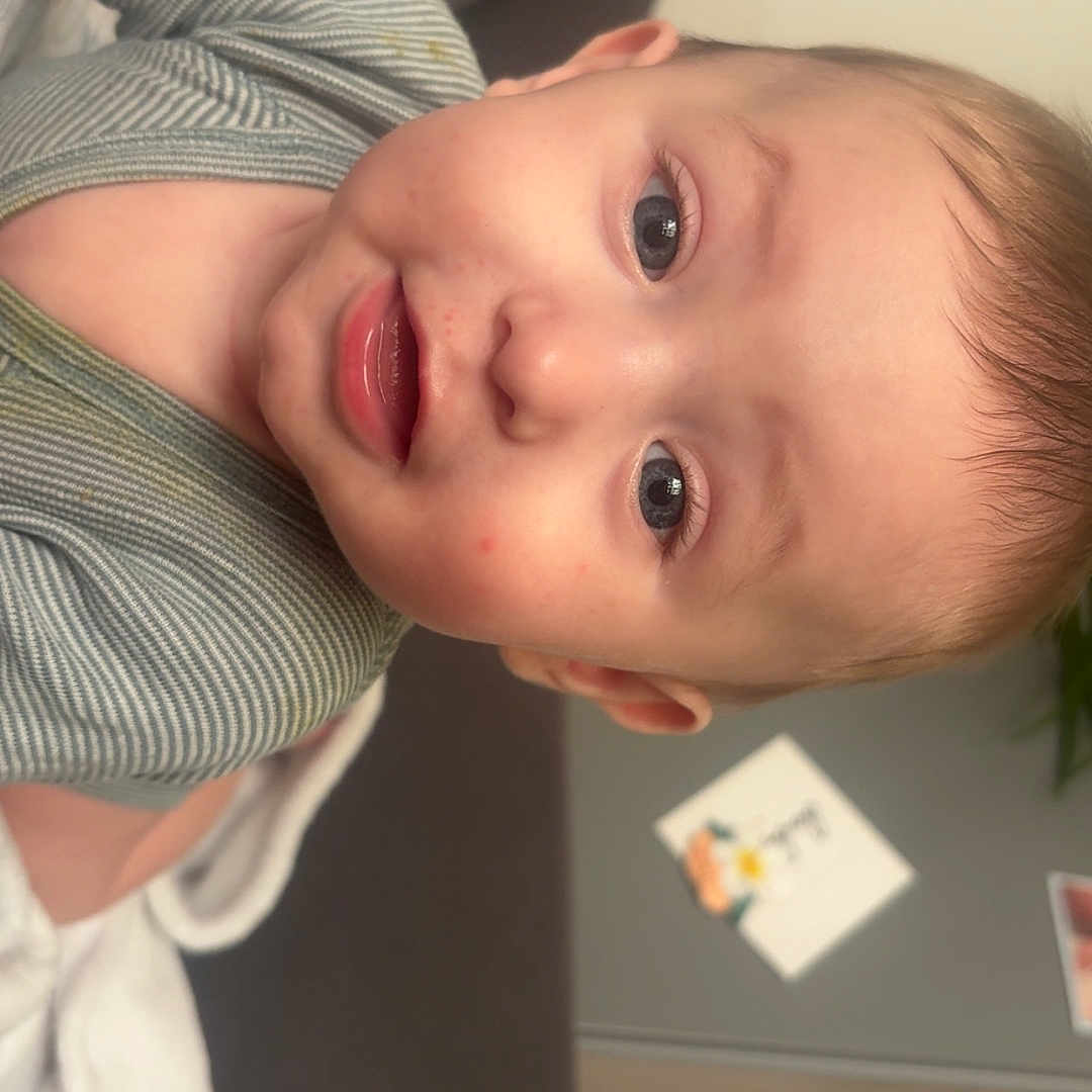 Ezio participe au concours pour gagner de l'argent avec cette photo : baby, blanket, child, closeup, clothing, couch, cute, expression, eyes, face, home, indoor, infant, mouth, portrait, skin, smile, soft, striped, young