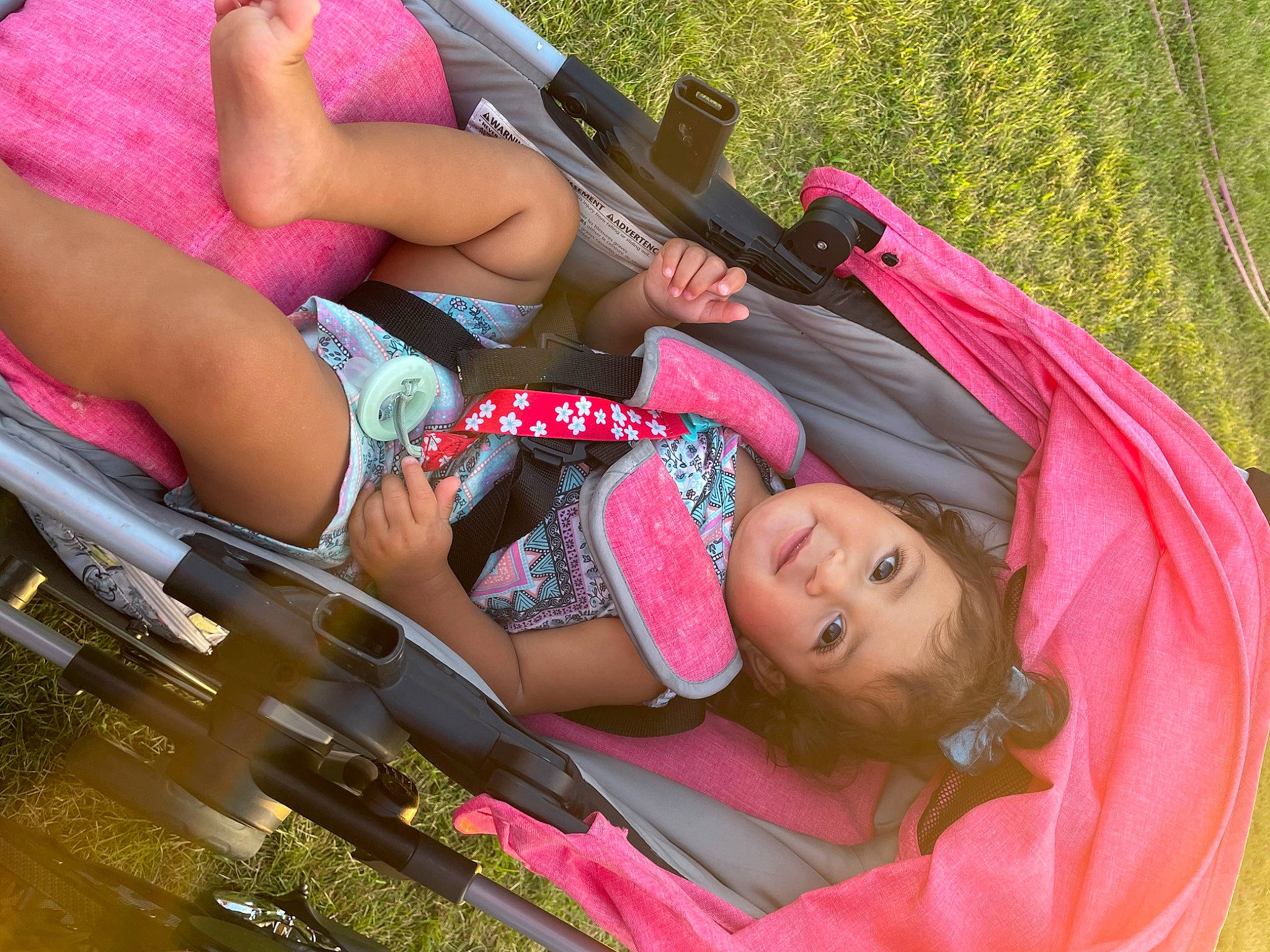 Lydia is registered to the contest to win money with this photo: automotive_design, automotive_exterior, bumper, child, cool, fun, grass, happy, human_leg, leisure, magenta, motor_vehicle, people_in_nature, person, pink, recreation, sitting, thigh, tree, vacation