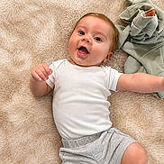 Kayson is registered to the contest to win money with this photo: baby, infant, white_onesie, grey_shorts, soft_blanket, smiling, happy, lying_down, cute, child, casual_clothing, indoors, cozy, toddler, playful, young_child, face, head, skin, expression