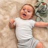 baby, infant, white_onesie, grey_shorts, soft_blanket, smiling, happy, lying_down, cute, child, casual_clothing, indoors, cozy, toddler, playful, young_child, face, head, skin, expression