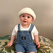Zao a rejoint le concours — aidez-le/la à gagner de superbes lots ! baby, beanie, casual_clothing, child, curious, cushion, cute, denim_overalls, face, hat, headwear, indoor, leaf_pattern, neutral_background, portrait, sitting, smiling, toddler, white_tshirt, young_child