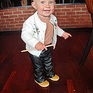 Mia participe au concours pour gagner de l'argent avec cette photo : toddler, child, smiling, standing, indoor, wooden_floor, cardigan, pants, shoes, stick, brick_wall, chair, person, happy, cute, blue_eyes, blond_hair, casual_clothing, portrait, small_child